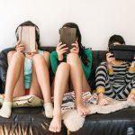 Three kids holding tablets sit on a couch