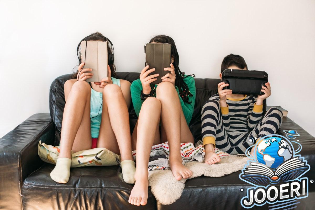 Three kids holding tablets sit on a couch