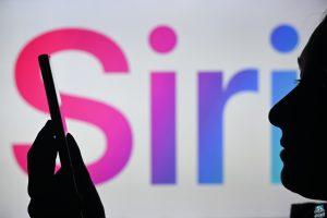 An image of a woman holding a cell phone in front of the Siri logo displayed on a computer screen.